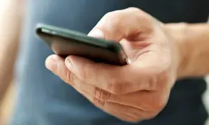 En hand håller en mobiltelefon. Kanske funderar personen på vad betyder tre punkter i sms, eller så väntar den på ett svar.
