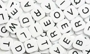 Vita bokstavsbrickor med svarta bokstäver, som i ett spel. Vad betyder synonym? Bokstäverna bildar ord som "love" och "are".