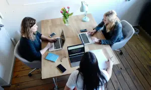 Tre kvinnor arbetar vid ett träbord. En bok med titeln "Empowered women" ligger på bordet, vilket antyder att de kanske diskuterar en metod för examensarbete.