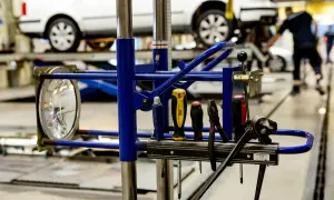 Verktyg redo för arbete efter punkt. En strålkastare och diverse verktyg hänger på en blå ställning framför bilar på en verkstad.