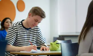 En ung man skriver koncentrerat i ett anteckningsblock. Ett **subjektivt exempel** på fokus i klassrummet.