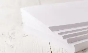 En hög med A4-papper på ett vitt träbord. Tänk hur många ord som ryms på en A4!