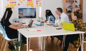 Teamwork i en svensk workshop. Fem personer sitter runt ett bord med laptops och post-it-lappar på väggen.