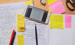 En mobiltelefon visar en text på arabiska, omgiven av anteckningar och post-it-lappar. En sammanfattning av uppsatsen kan finnas bland dessa.