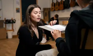 En lärare förklarar hur man skriver en rapport för en elev. I bakgrunden hänger gitarrer.