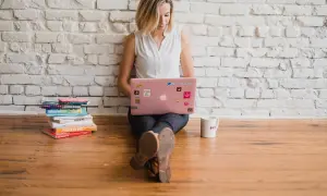 Kvinna med rosa laptop och böcker. Hon arbetar med text, kanske som en skribent som använder fikonspråk synonymt med kreativt skrivande.