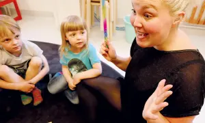 En pedagog leder barnen i rim och ramsor för språkutveckling. Hon håller i en färgglad stav.