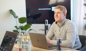 Man i grå tröja vid laptop, med vattenflaskor och en läskburk. En skärm visar text, som ett referat exempel artikel.