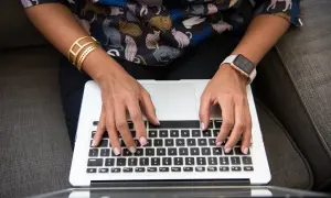 Person med kattmönstrad tröja och smycken skriver på en laptop. Ett resonerande text exempel på hur man kan beskriva en bild.