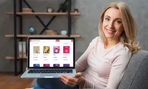 Glad kvinna visar sin laptop med en konst-webbshop. Hon bläddrar bland tavlor och parfymflaskor i webbshopen.