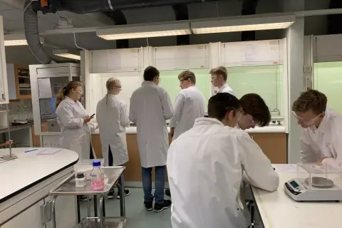 Elever i labbrockar har en diskussion labbrapport vid bänkar i ett kemilabb.