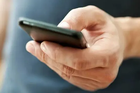 En hand håller en mobiltelefon. Kanske funderar personen på vad betyder tre punkter i sms, eller så väntar den på ett svar.