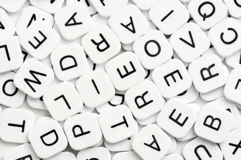 Vita bokstavsbrickor med svarta bokstäver, som i ett spel. Vad betyder synonym? Bokstäverna bildar ord som "love" och "are".