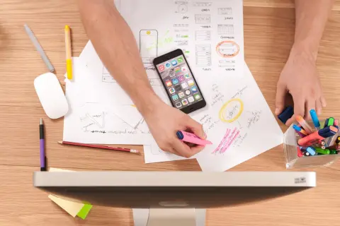 Person arbetar med en uppsats, omger sig med papper, en mobiltelefon och pennor. Resultat uppsats-idéer tar form.