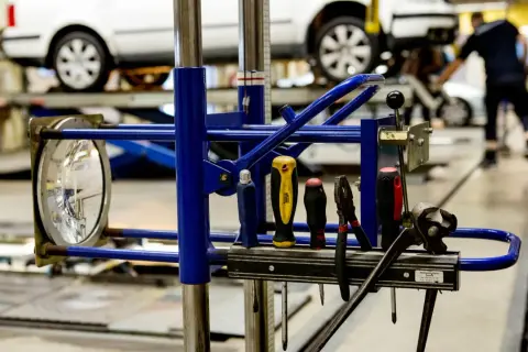 Verktyg redo för arbete efter punkt. En strålkastare och diverse verktyg hänger på en blå ställning framför bilar på en verkstad.