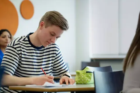 En ung man skriver koncentrerat i ett anteckningsblock. Ett **subjektivt exempel** på fokus i klassrummet.