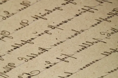 Detaljerad vy av handskriven text på gammalt papper. Texten är skriven med bläck och bildar rader som följer linjer. Det är svårt att tyda exakt vad som står, men det ger en känsla av ett gammalt referat.