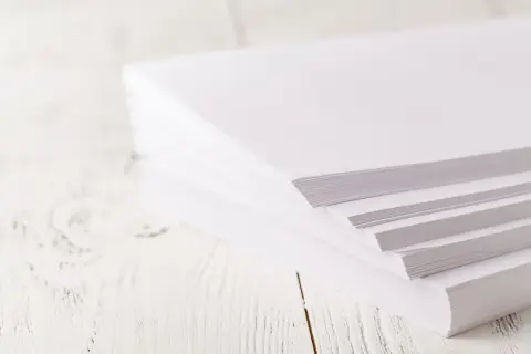 En hög med A4-papper på ett vitt träbord. Tänk hur många ord som ryms på en A4!
