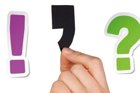En hand håller ett svart semikolon mellan ett lila utropstecken och ett grönt frågetecken.