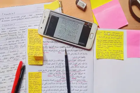En mobiltelefon visar en text på arabiska, omgiven av anteckningar och post-it-lappar. En sammanfattning av uppsatsen kan finnas bland dessa.