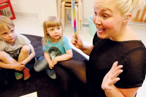 En pedagog leder barnen i rim och ramsor för språkutveckling. Hon håller i en färgglad stav.