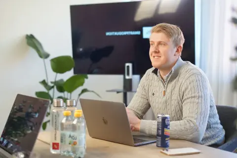 Man i grå tröja vid laptop, med vattenflaskor och en läskburk. En skärm visar text, som ett referat exempel artikel.
