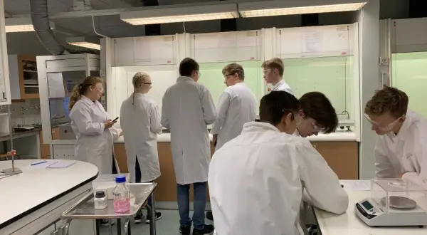 Elever i labbrockar har en diskussion labbrapport vid bänkar i ett kemilabb.
