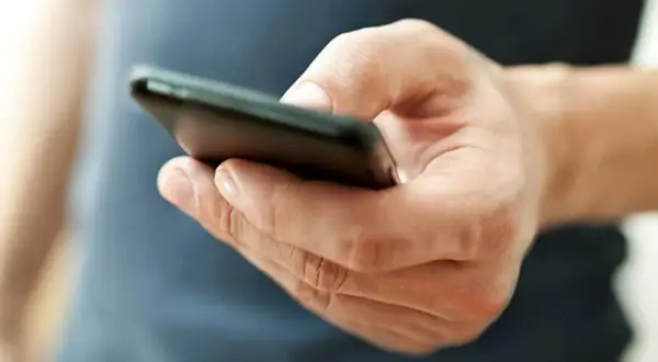 En hand håller en mobiltelefon. Kanske funderar personen på vad betyder tre punkter i sms, eller så väntar den på ett svar.