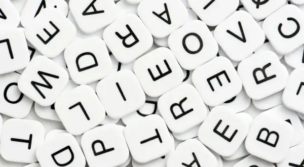 Vita bokstavsbrickor med svarta bokstäver, som i ett spel. Vad betyder synonym? Bokstäverna bildar ord som "love" och "are".