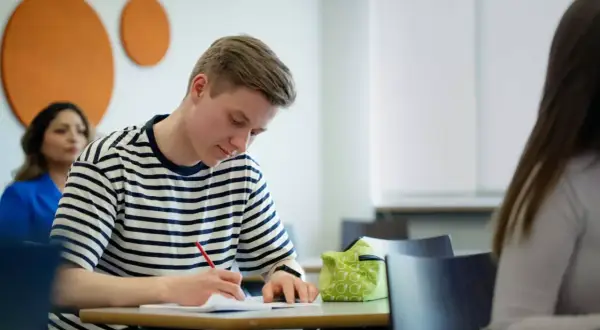 En ung man skriver koncentrerat i ett anteckningsblock. Ett **subjektivt exempel** på fokus i klassrummet.