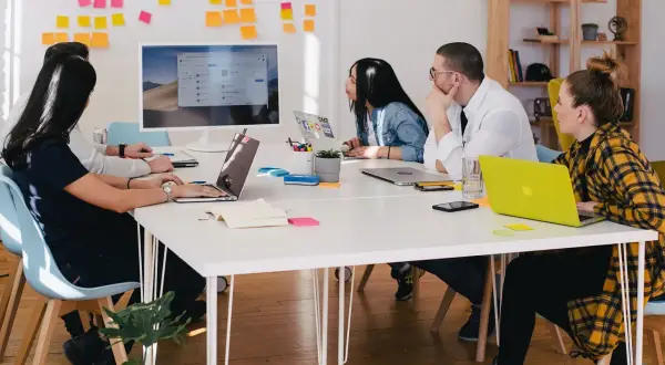 Teamwork i en svensk workshop. Fem personer sitter runt ett bord med laptops och post-it-lappar på väggen.
