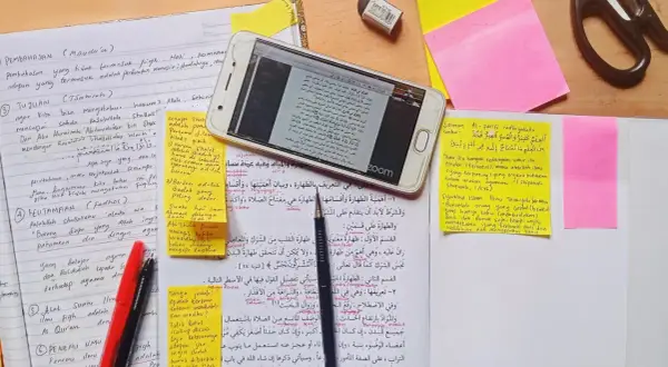 En mobiltelefon visar en text på arabiska, omgiven av anteckningar och post-it-lappar. En sammanfattning av uppsatsen kan finnas bland dessa.