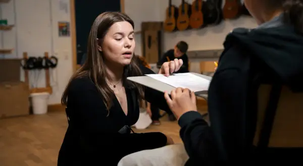 En lärare förklarar hur man skriver en rapport för en elev. I bakgrunden hänger gitarrer.