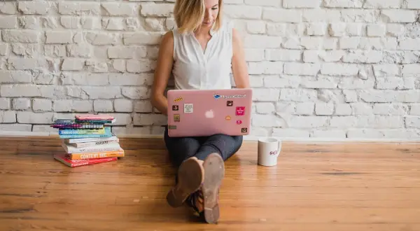 Kvinna med rosa laptop och böcker. Hon arbetar med text, kanske som en skribent som använder fikonspråk synonymt med kreativt skrivande.