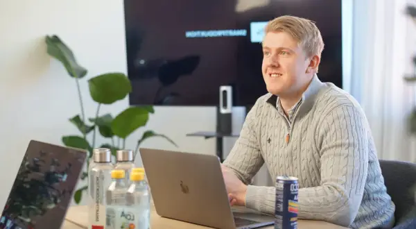 Man i grå tröja vid laptop, med vattenflaskor och en läskburk. En skärm visar text, som ett referat exempel artikel.