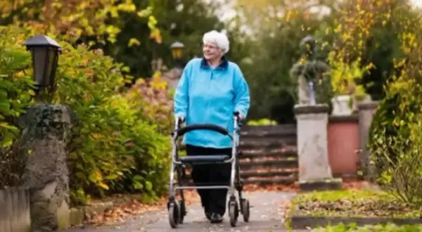 Äldre kvinna med vit frisyr går med en rullator i en vacker höstpark.