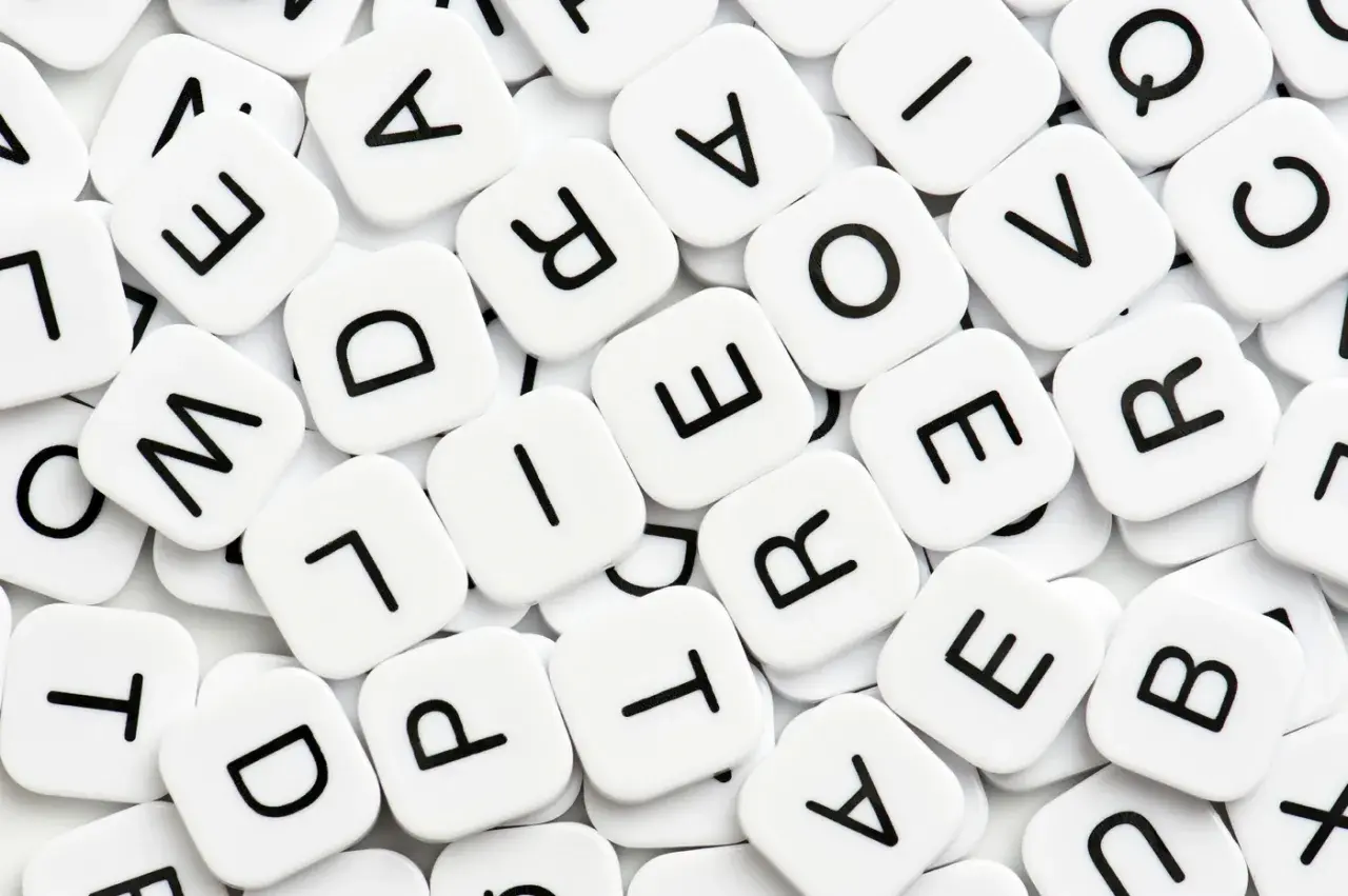 Vita bokstavsbrickor med svarta bokstäver, som i ett spel. Vad betyder synonym? Bokstäverna bildar ord som "love" och "are".