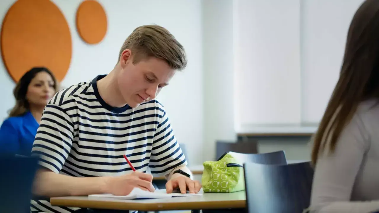 En ung man skriver koncentrerat i ett anteckningsblock. Ett **subjektivt exempel** på fokus i klassrummet.