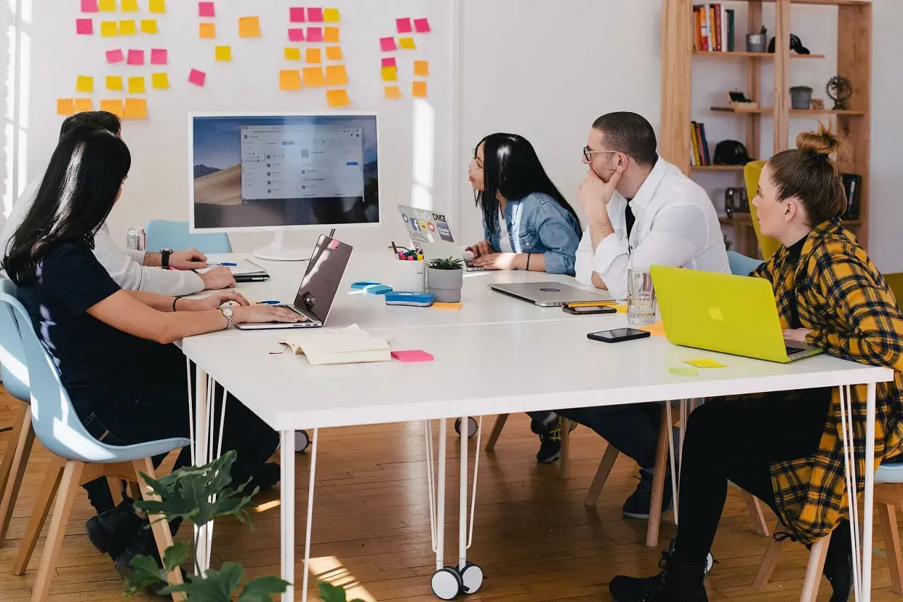 Teamwork i en svensk workshop. Fem personer sitter runt ett bord med laptops och post-it-lappar på väggen.