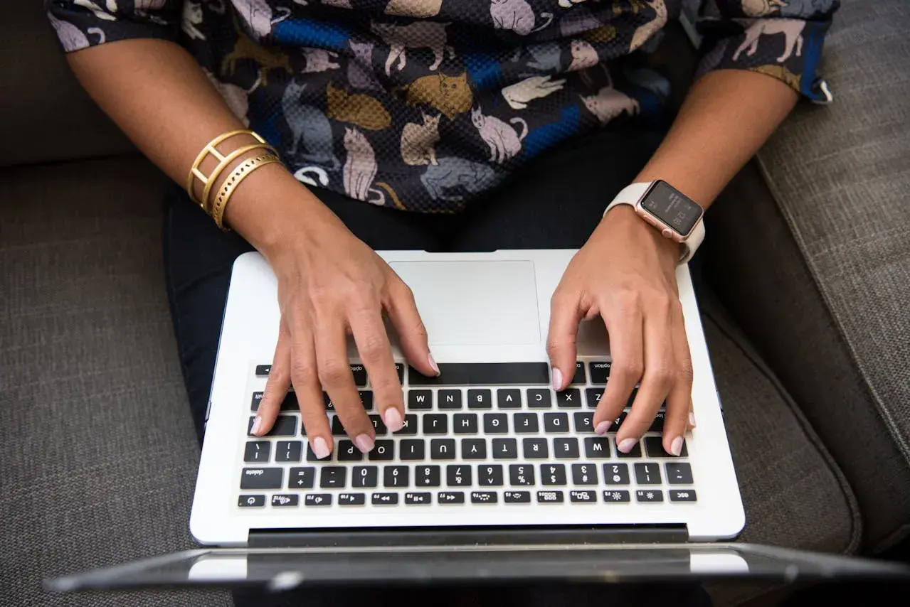 Person med kattmönstrad tröja och smycken skriver på en laptop. Ett resonerande text exempel på hur man kan beskriva en bild.