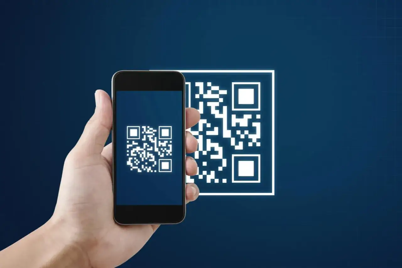 En hand h&aring;ller en mobiltelefon f&ouml;r att skanna en QR-kod. En annan, st&ouml;rre QR-kod syns i bakgrunden.