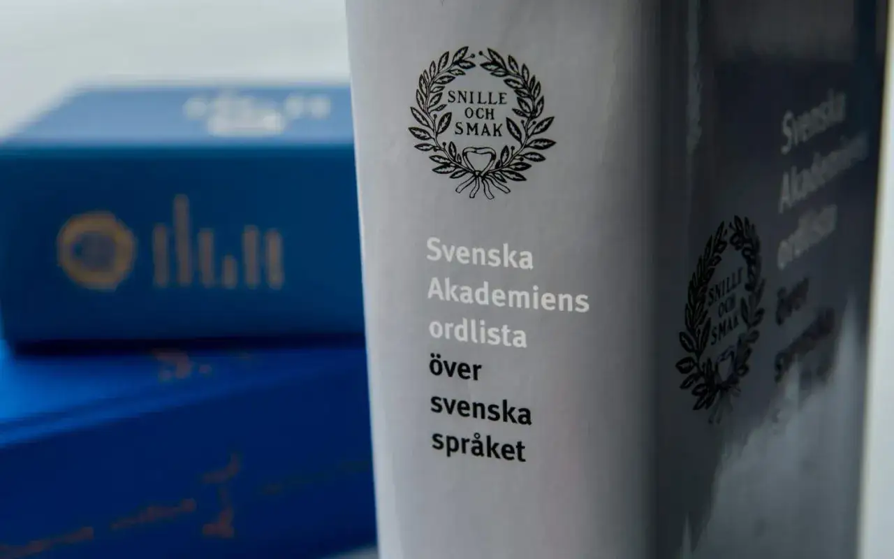 Svenska Akademiens ordlista &ouml;ver svenska spr&aring;ket. Bl&aring; askar med gul text syns i bakgrunden, som om de v&auml;ntar p&aring; att f&aring; veta vart eller blev.