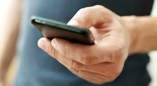 En hand håller en mobiltelefon. Kanske funderar personen på vad betyder tre punkter i sms, eller så väntar den på ett svar.