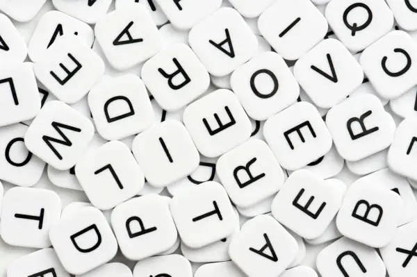 Vita bokstavsbrickor med svarta bokstäver, som i ett spel. Vad betyder synonym? Bokstäverna bildar ord som "love" och "are".