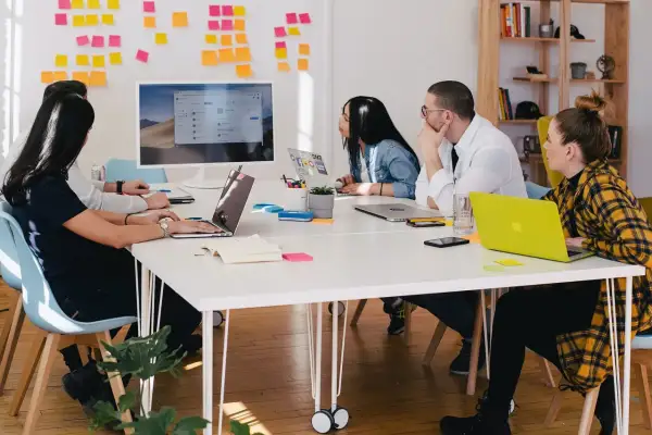 Teamwork i en svensk workshop. Fem personer sitter runt ett bord med laptops och post-it-lappar på väggen.