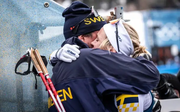 Två skidåkare i svenska färger kramas. Mannen har mössa med texten "SWE" och kvinnan har pannband. De står fram emot varandra i en varm omfamning.